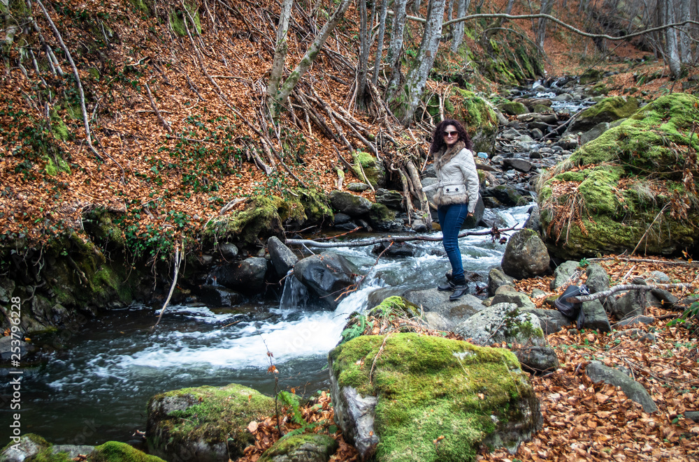 Woman stands by the small river in the forest. End of winter and beginning of the spring