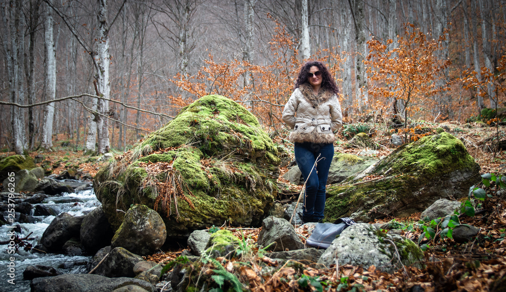 Naklejka premium Woman stands by the small river in the forest. End of winter and beginning of the spring