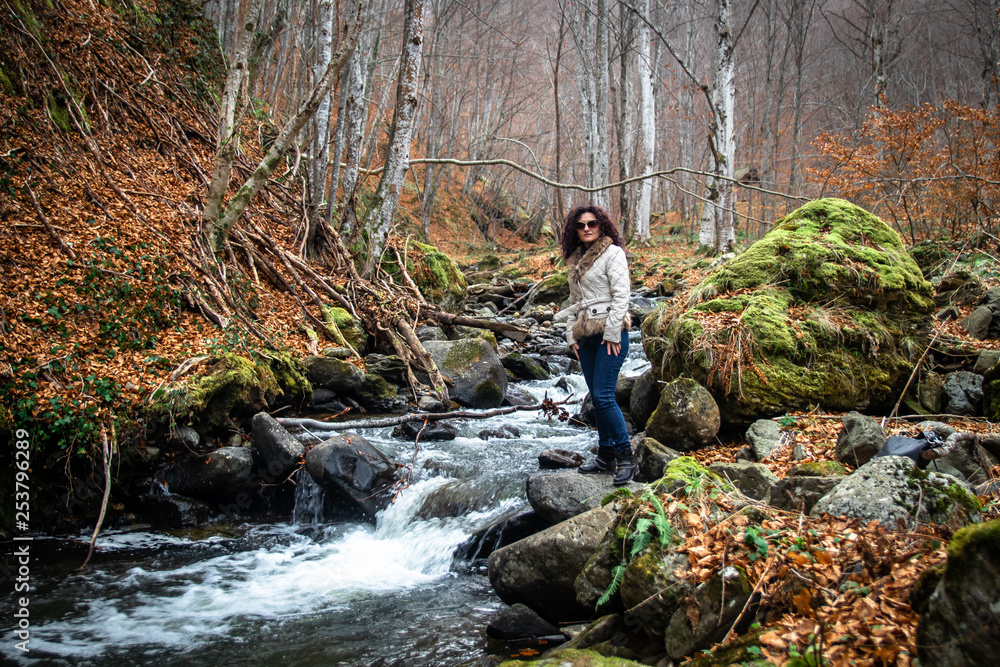 Woman stands by the small river in the forest. End of winter and beginning of the spring