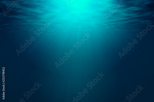 Deep blue sea with rays of sunlight, ocean surface seen from underwater. Background texture with copy space for text or product display.