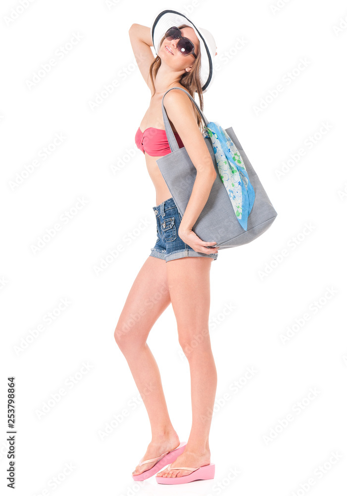 Bikini vacation holidays young woman standing with bag, isolated on white background in studio, full body length. Happy girl in bikini swimsuit, sunglasses and sun hat. Bikini vacation holidays young woman standing with bag, isolated on white background in studio, full body length. Happy girl in bikini swimsuit, sunglasses and sun hat.