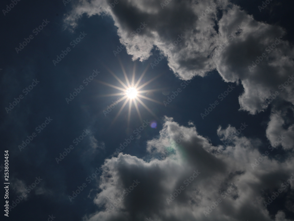A picture of bright sun among bright clouds on a sunny day.