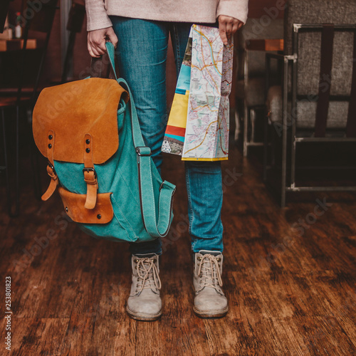 Crop photo of young woman feet girl traveler in jeans and boots with backpack and map indoors
