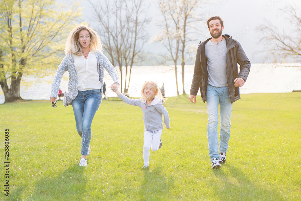 Happy father, mother and little girl running alongside lake and enjoying on a beautiful sunny day. Happy father, mother and little girl running alongside lake and enjoying on a beautiful sunny day.