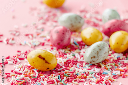 Easter chocolate eggs candy with colorful sprinkles on a pastel pink background, creative easter concept, top view