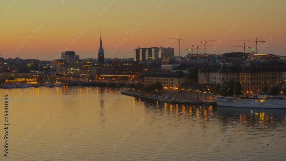Aerial shot of town viewed from bay, recreational area people sitting on benches and by the edge of quay, church spire and traffic in background. Aerial shot of town viewed from bay, recreational area people sitting on benches and by the edge of quay, church spire and traffic in background.