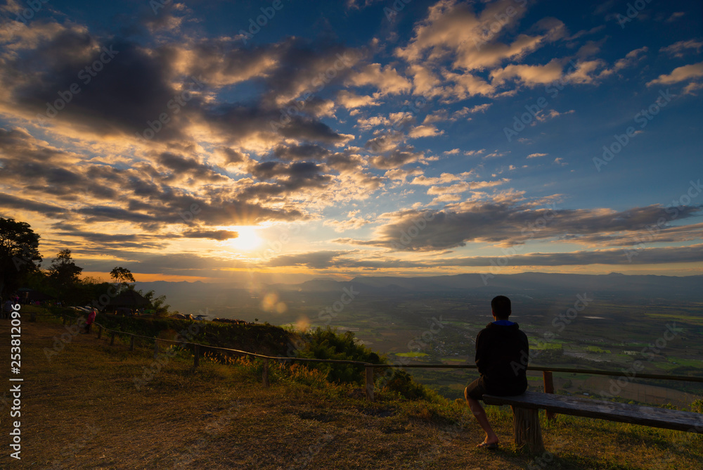 Backside of a man sit on wooden bench looking at the sun while sunset over the mountains