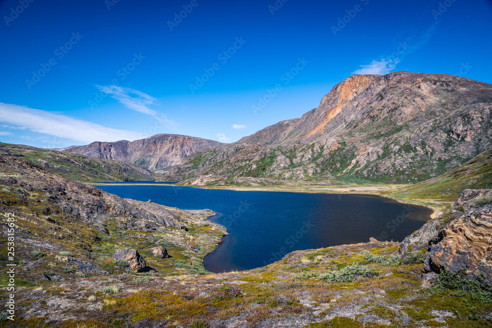 Hiking in the arctic - the Arctic Circle Trail (ACT) along a crystalline lake during summer in Greenland with beautiful landscape views, grass, mountains, blue sky