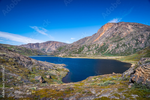 Hiking in the arctic - the Arctic Circle Trail (ACT) along a crystalline lake during summer in Greenland with beautiful landscape views, grass, mountains, blue sky