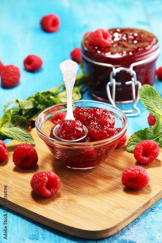 raspberry jam with fresh raspberries and mint. marmalade on spoon and jar on blue raspberry jam with fresh raspberries and mint. marmalade on spoon and jar on blue