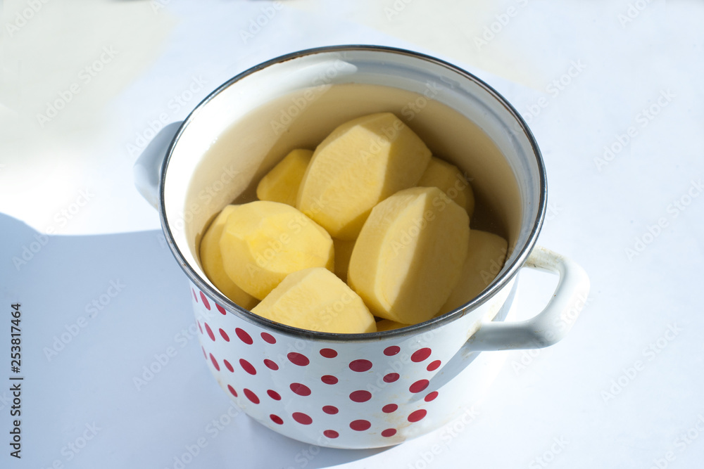 peeled raw potatoes in a pot on a white background peeled raw potatoes in a pot on a white background