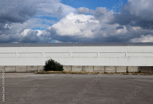 Wallpaper Mural White industrial warehouse building with a cement surrounding wall and a large asphalt road under a blue sky with many clouds. Background for copy space Torontodigital.ca