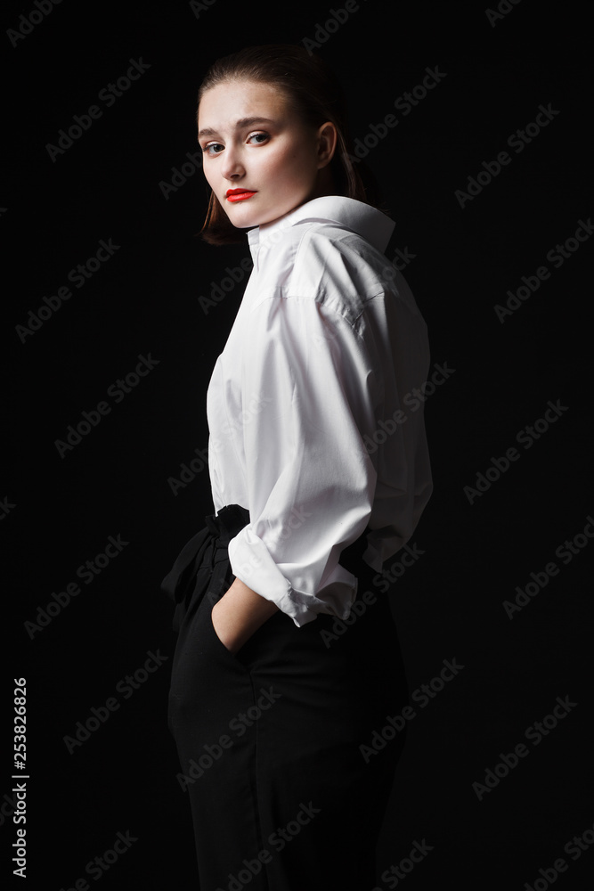 Portrait of an elegant young woman in a white shirt and black pants. Interesting studio light Portrait of an elegant young woman in a white shirt and black pants. Interesting studio light