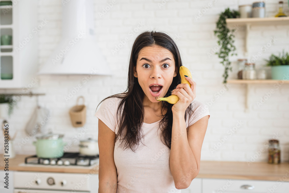 Attractive surprised woman is holding banana like a mobile phone, funny concept Attractive surprised woman is holding banana like a mobile phone, funny concept