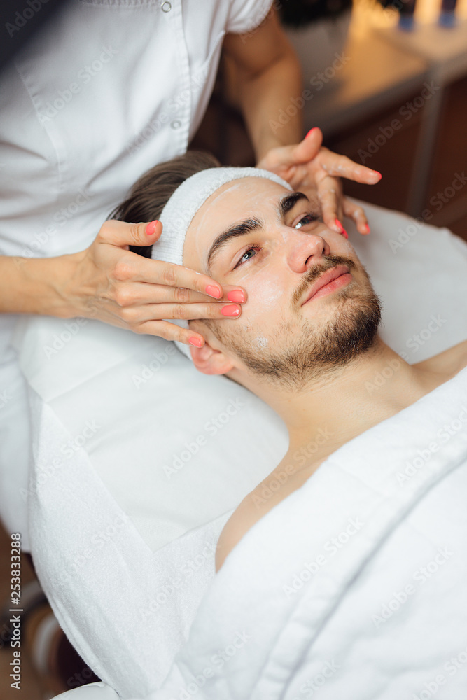 Fototapeta premium Unshaven man having cosmetic mask care in spa salon, side, top view - Image