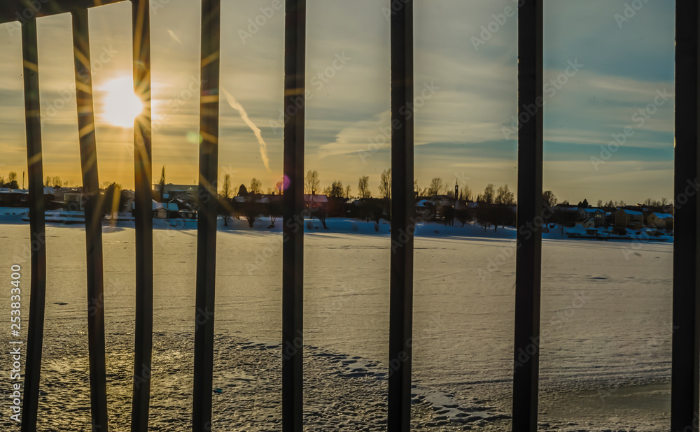 Sun flares through the railing and reflection on the frozen river