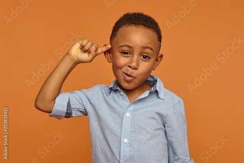 Foto Are you out of your mind? Horizontal shot of handsome emotional Afro American little boy in shirt twisting fore finger at his temple