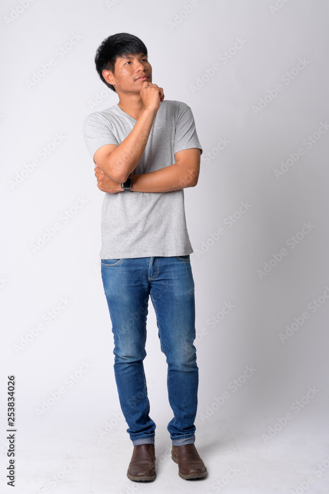 Full body shot of young Asian man thinking Full body shot of young Asian man thinking