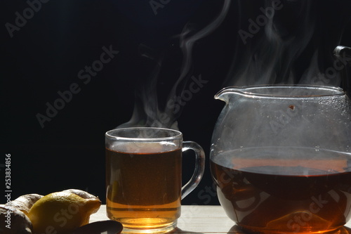 smoke rising from a cup of ginger tea with a teapot on a wooden table in front of a black background