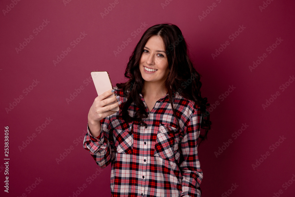 Photo of nice young woman holding and using smartphone isolated over the dark pink background Photo of nice young woman holding and using smartphone isolated over the dark pink background