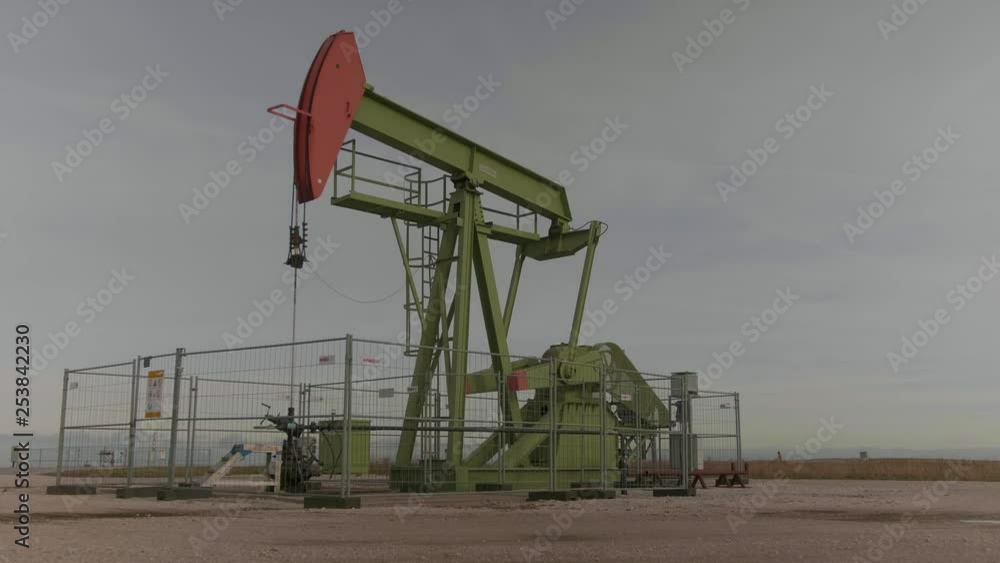 steady shot of a green/orange oil derrick moving steady shot of a green/orange oil derrick moving