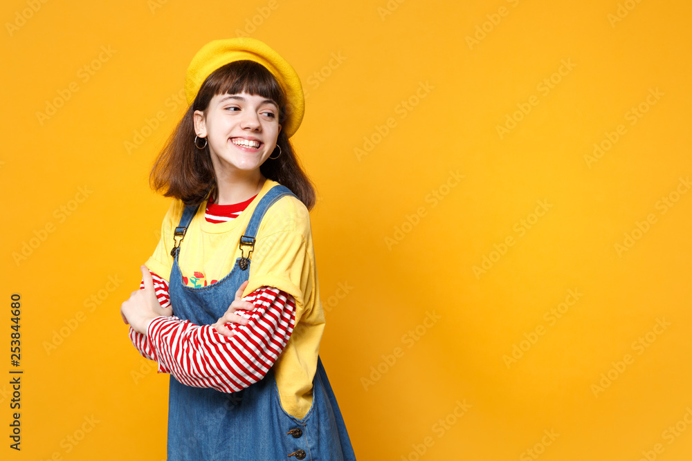 Pretty girl teenager in french beret, denim sundress holding hands folded, looking aside isolated on yellow wall background in studio. People sincere emotions, lifestyle concept. Mock up copy space. Pretty girl teenager in french beret, denim sundress holding hands folded, looking aside isolated on yellow wall background in studio. People sincere emotions, lifestyle concept. Mock up copy space.