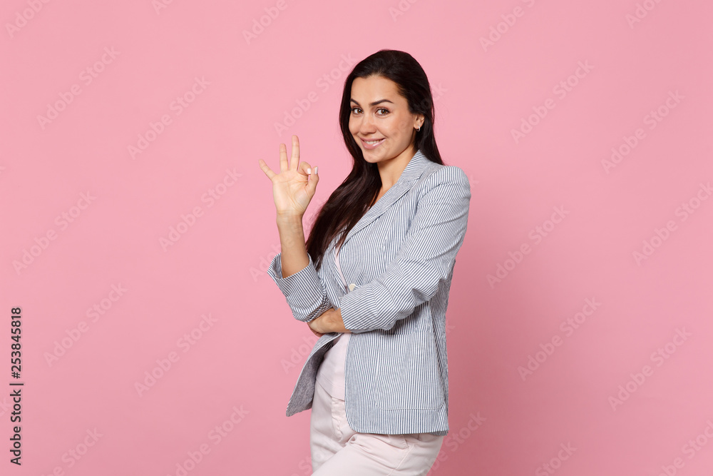 Portrait of smiling attractive young woman in striped jacket standing, showing OK gesture isolated on pink pastel background in studio. People sincere emotions, lifestyle concept. Mock up copy space. Portrait of smiling attractive young woman in striped jacket standing, showing OK gesture isolated on pink pastel background in studio. People sincere emotions, lifestyle concept. Mock up copy space.