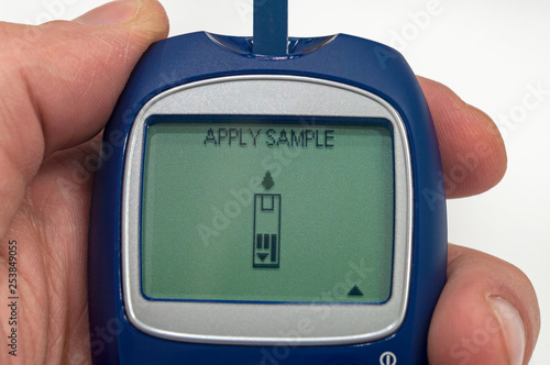 Portable glucometer ready for blood sample analysis in male hand on white background. photo