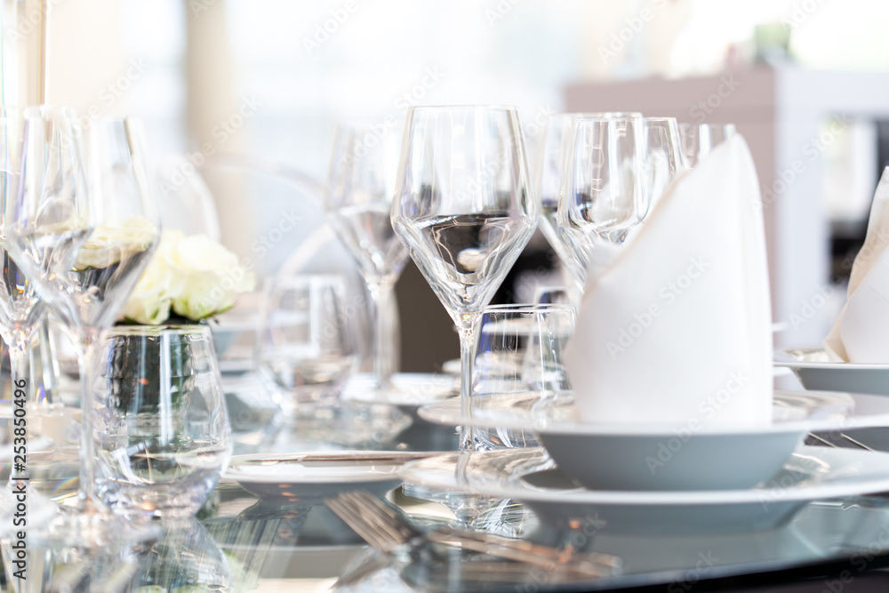 Detail of modern banquet setting on glass table. Blurry background.