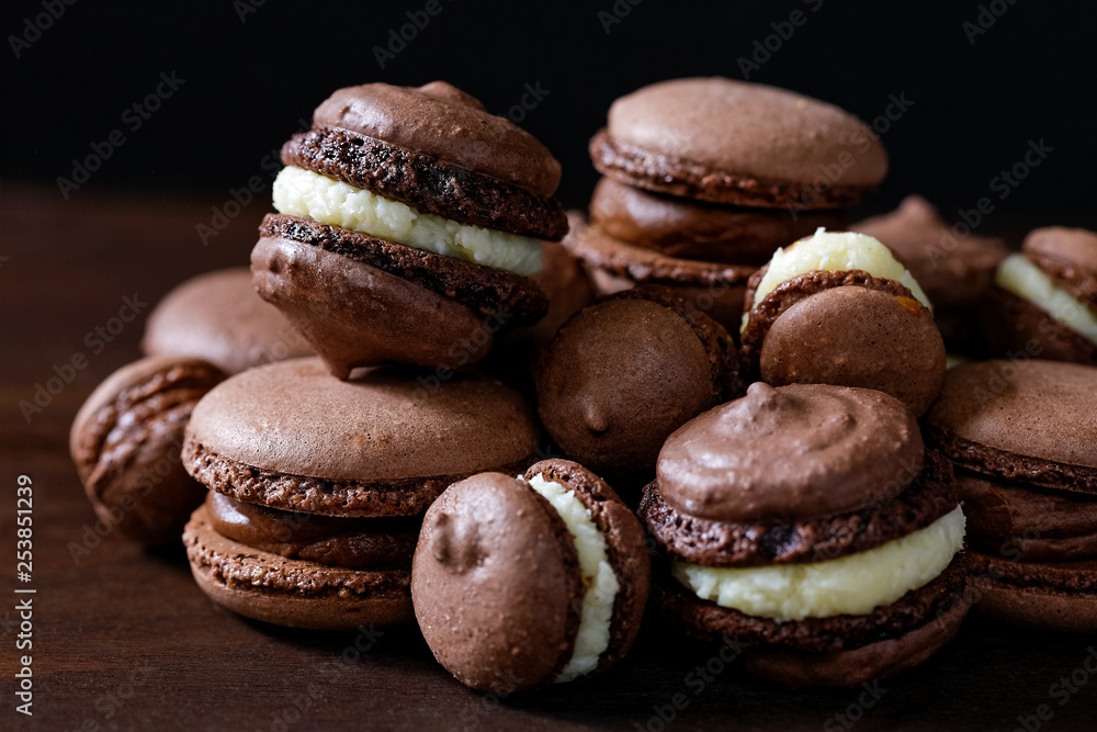 Chocolate macarons of various sizes. Brown background.