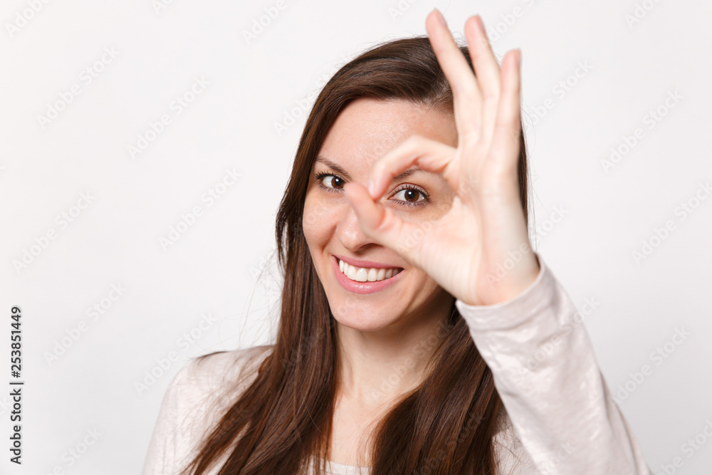 Close up portrait of smiling young woman in light clothes looking camera showing OK gesture isolated on white wall background in studio. People sincere emotions, lifestyle concept. Mock up copy space. Close up portrait of smiling young woman in light clothes looking camera showing OK gesture isolated on white wall background in studio. People sincere emotions, lifestyle concept. Mock up copy space.