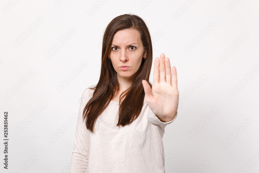 Portrait of serious concerned young woman in light clothes showing stop gesture with palm isolated on white wall background in studio. People sincere emotions, lifestyle concept. Mock up copy space. Portrait of serious concerned young woman in light clothes showing stop gesture with palm isolated on white wall background in studio. People sincere emotions, lifestyle concept. Mock up copy space.