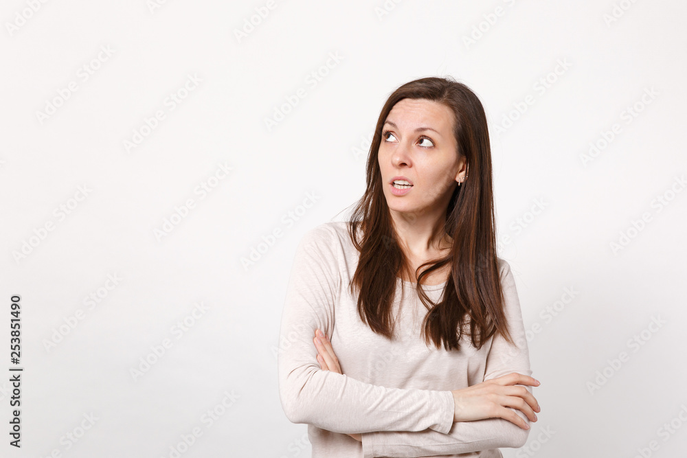 Portrait of puzzled pensive young woman in light clothes looking up, holding hands crossed isolated on white wall background in studio. People sincere emotions, lifestyle concept. Mock up copy space. Portrait of puzzled pensive young woman in light clothes looking up, holding hands crossed isolated on white wall background in studio. People sincere emotions, lifestyle concept. Mock up copy space.