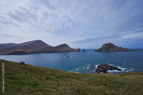 Epic colorful landscape of wild nordic or scandinavian coastline without trees with atlantic ocean, mountains, high cliffs in island Vagar in Faroe island taken in sunny, cloudy and windy summer day. 