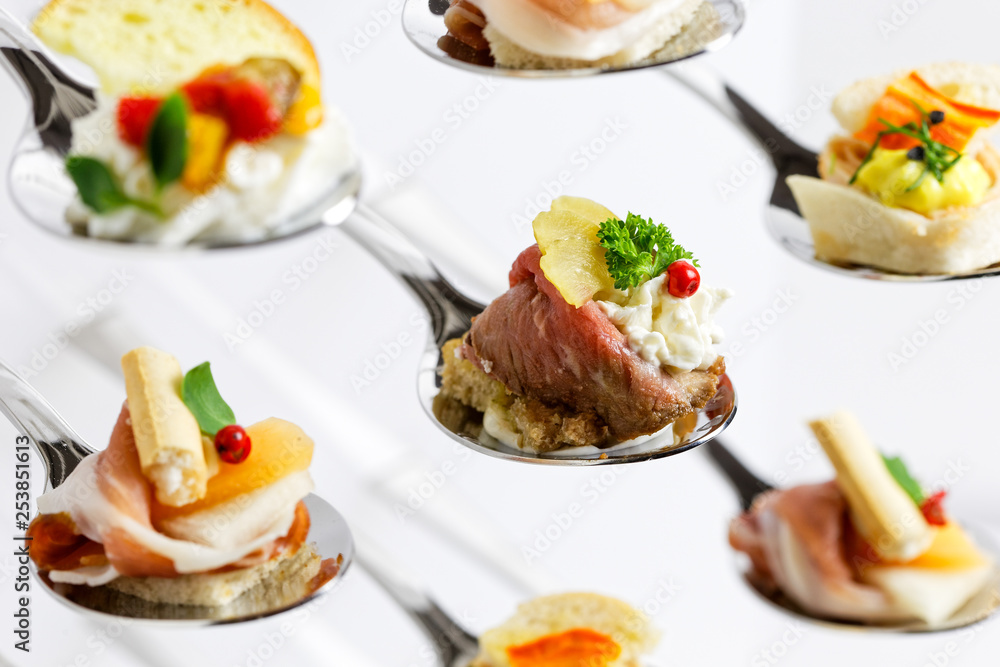 Closeup of mixed canapes on metal spoons. White background.