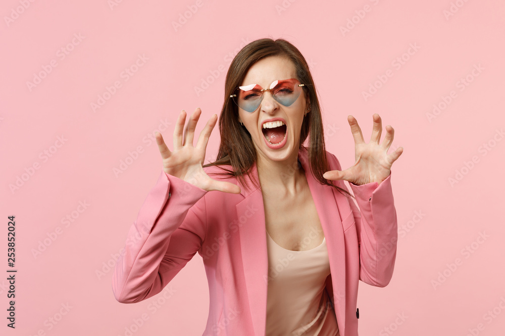 Crazy young woman in heart glasses shouting growling like animal, making cat claws gesture isolated on pastel pink background in studio. People sincere emotions, lifestyle concept. Mock up copy space. Crazy young woman in heart glasses shouting growling like animal, making cat claws gesture isolated on pastel pink background in studio. People sincere emotions, lifestyle concept. Mock up copy space.