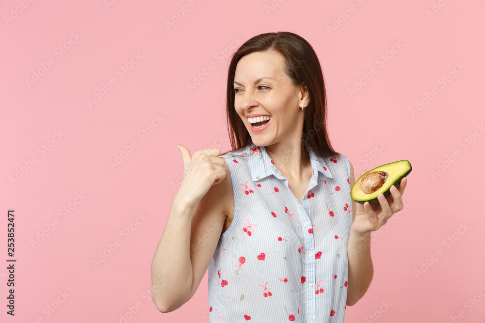 Laughing young woman in summer clothes pointing thumb aside hold half of fresh ripe avocado fruit isolated on pink pastel background. People vivid lifestyle relax vacation concept. Mock up copy space. Laughing young woman in summer clothes pointing thumb aside hold half of fresh ripe avocado fruit isolated on pink pastel background. People vivid lifestyle relax vacation concept. Mock up copy space.