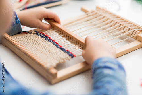 A little girl learns process to weave thick threads. Hands close up.