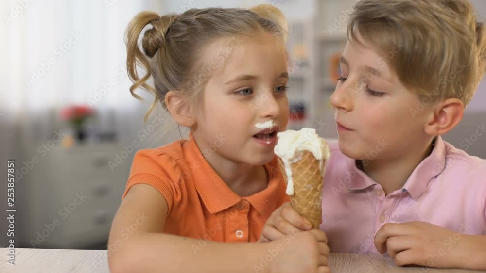Adorable brother and sister eating ice-cream together sitting home table, food Adorable brother and sister eating ice-cream together sitting home table, food