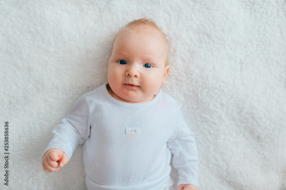Adorable lovely newborn male baby with blue eyes lifestyle indoor portrait from above. Cute child with hands apart lying on back in pijama on bed at home. Little child with emotional face rest on sofa Adorable lovely newborn male baby with blue eyes lifestyle indoor portrait from above. Cute child with hands apart lying on back in pijama on bed at home. Little child with emotional face rest on sofa