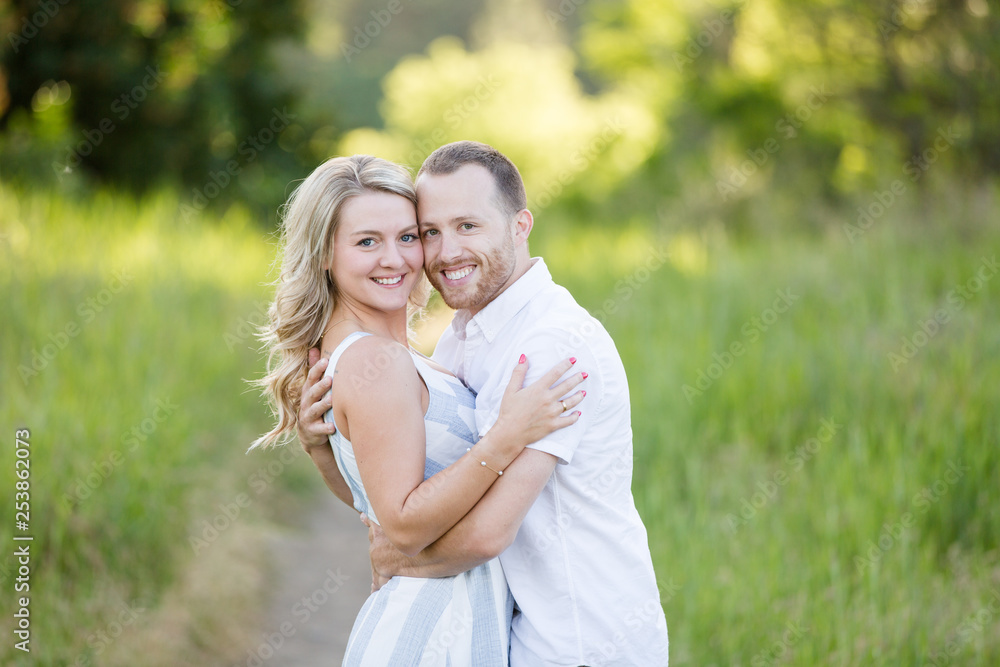 Attractive young couple embracing and smiling in green grass field Attractive young couple embracing and smiling in green grass field