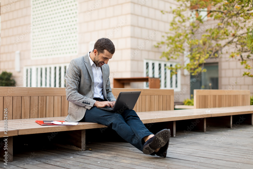 Smiling businessman sitting on a bench using laptop Smiling businessman sitting on a bench using laptop