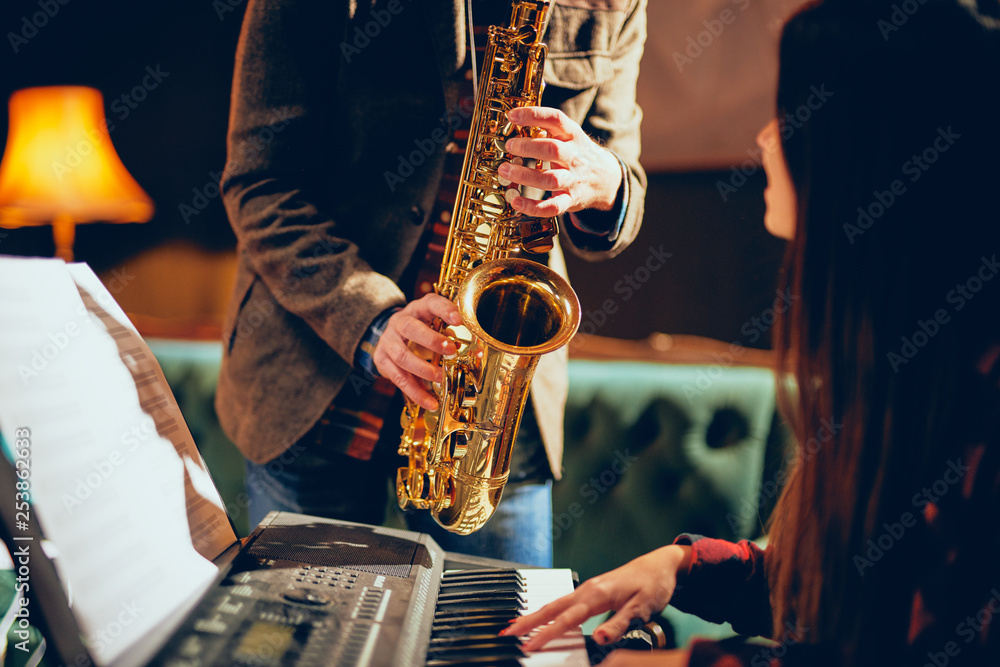 Obraz premium Caucasian man playing saxophone in home studio while young talented woman playing clavier.