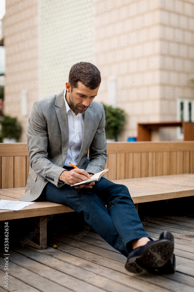 Businessman sitting on a bench writing into diary Businessman sitting on a bench writing into diary