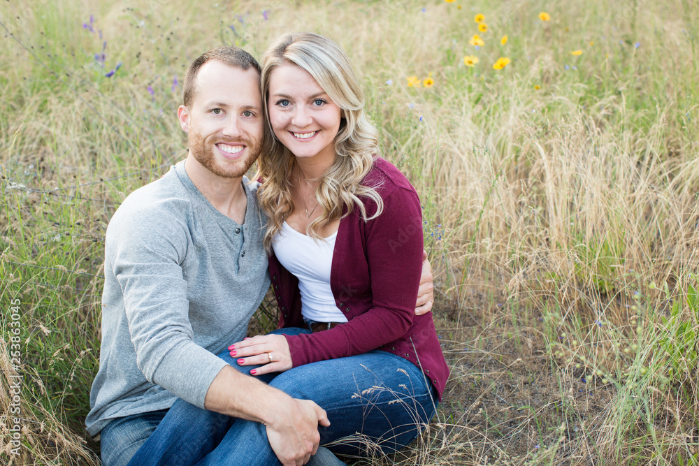 Attractive young couple smiling at camera sitting in wild flowers and grass Attractive young couple smiling at camera sitting in wild flowers and grass