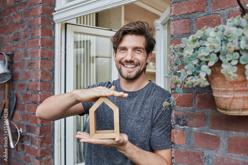 Portrait of smiling man at house entrance holding house model photo