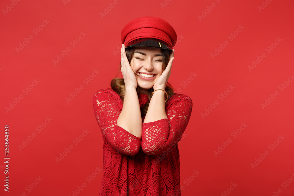 Portrait of smiling young woman in lace dress and cap keeping eyes closed, putting hands on face isolated on bright red wall background. People sincere emotions, lifestyle concept. Mock up copy space. Portrait of smiling young woman in lace dress and cap keeping eyes closed, putting hands on face isolated on bright red wall background. People sincere emotions, lifestyle concept. Mock up copy space.