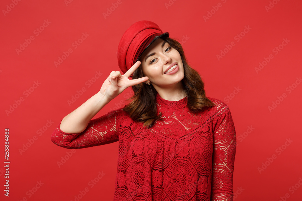 Portrait of smiling young woman in lace dress, cap looking camera showing victory sign isolated on bright red wall background in studio. People sincere emotions, lifestyle concept. Mock up copy space. Portrait of smiling young woman in lace dress, cap looking camera showing victory sign isolated on bright red wall background in studio. People sincere emotions, lifestyle concept. Mock up copy space.