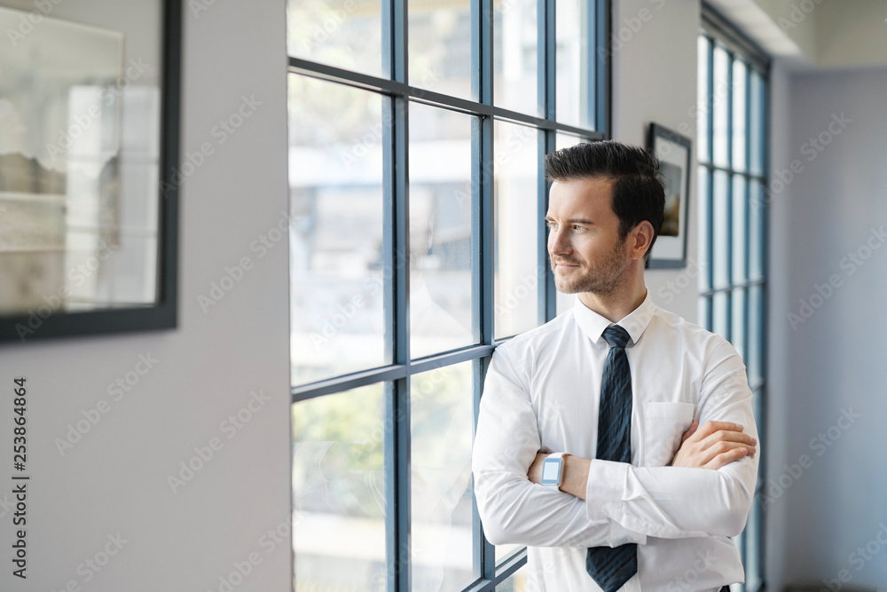Confident businessman standing in office looking out of window Confident businessman standing in office looking out of window