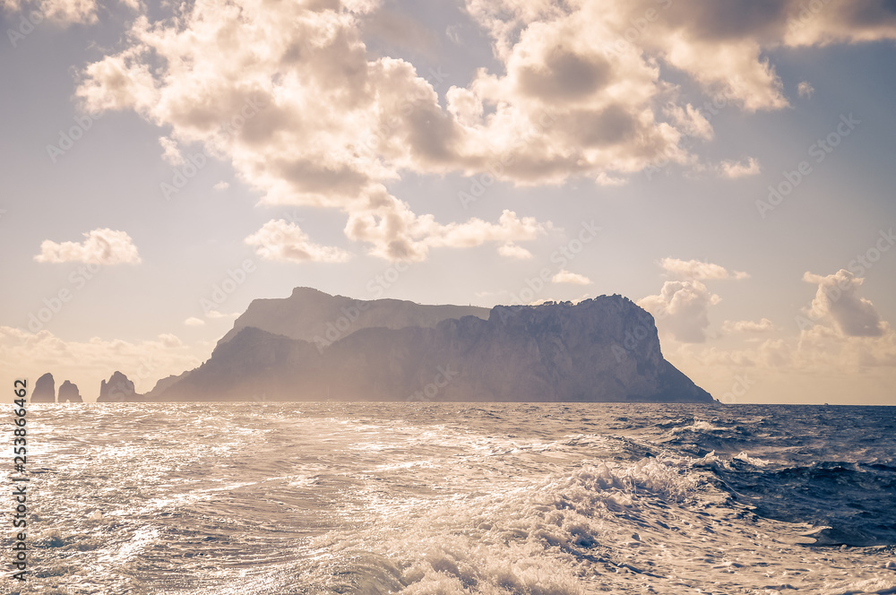 The Faraglioni of Capri island silhouette behind the wake of a boat, Italy